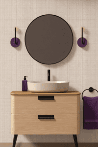A minimalist mid-century modern bathroom vanity featuring a light wood finish and sleek black accents. The vanity includes a rounded ceramic basin and a matching black faucet. Above it, a large circular mirror complements the geometric wall sconces in vibrant purple, paired with a textured beige background. A purple towel and decorative elements enhance the design's bold yet cohesive aesthetic.
